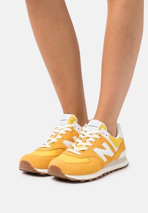 Baskets en daim jaune avec des accents blancs et des lacets blancs. Caractérisées par un bout arrondi et une semelle rembourrée. Marquage sur la languette et le côté.