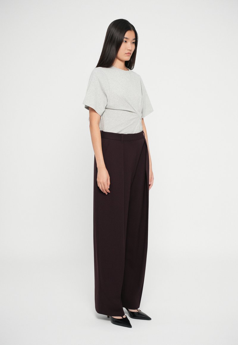 Top grigio a maniche corte con nodo abbinato a pantaloni a vita alta e gamba larga di un intenso bordeaux scuro. La modella indossa scarpe nere a punta. Design semplice e pulito.