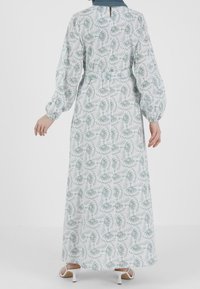 Pitkä, vaalea kankainen mekko, jossa on valkoinen tausta ja vihreä lehtikuvio. Puffihihat ja avainaukko takana.