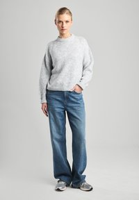 Light gray knit sweater with a crew neckline, paired with loose blue denim jeans and gray athletic shoes. Soft texture, relaxed fit.