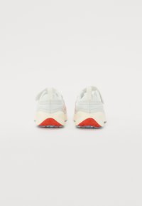 Zapatillas elegantes con parte superior en gris claro, tela suave, acento rojo en el talón y suela de goma crema con tracción azul para estabilidad.