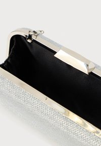 Clutch prateado metálico com exterior texturizado, ferragens prateadas e fecho brilhante. Interior em tecido preto, mostrando um amplo espaço de armazenamento.