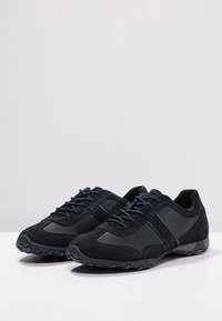 Czarne buty sportowe wykonane z zamszu i materiału syntetycznego, z kontrastującymi niebieskimi przeszyciami, sznurowanym przodem i teksturowaną podeszwą.