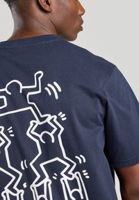 Camiseta de algodón azul marino con un gran gráfico blanco de figuras abstractas en poses dinámicas en la parte posterior, con mangas cortas y un corte clásico.
