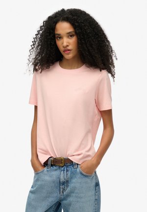 Light pink cotton t-shirt with a round neckline, short sleeves, and subtle embossed branding on the left chest. Worn with blue denim jeans.