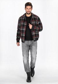 Schwarz-rotes kariertes Bomberjacke mit Kragen, getragen über einem schwarzen Shirt, kombiniert mit grauen Jeans und schwarzen schnürbaren Stiefeln.