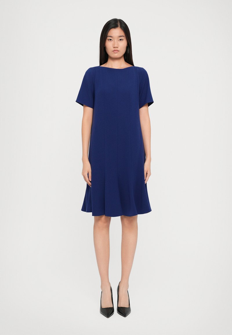 Rochie bleumarin până la genunchi, cu mâneci scurte, gât rotund și siluetă evazată. Material neted cu detalii subtile de cusături verticale.