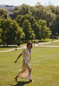 Light-colored, flowy dress featuring a short-sleeve shirt top and long skirt with wavy brown lines, set against a grassy park background.