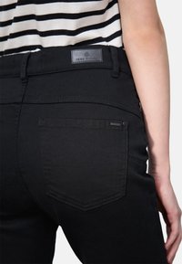 Jean en denim noir avec un design classique, une patch en cuir à la taille, et deux poches arrière avec des détails de couture discrets.