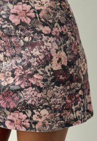 Ziedu apdruka uz denima svārkiem ar tumšu fonu, kurā redzami rozā, purpura un krēma ziedi. Auduma tekstūra ir nedaudz raupja, ar redzamām šuvēm.