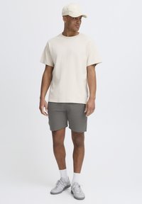 T-shirt beige à manches courtes, shorts gris, baskets gris clair et une casquette assortie. Look décontracté avec un design simple et une texture douce.