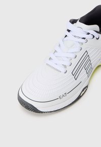 Pantofii sport albi, cu o suprafață texturată, accente din plasă și detalii negre. Au un logo distinct EA7 și o talpă din cauciuc cu un model.
