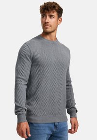 Pulover gri din tricot cu un model în zigzag, decolteu rotund, manșete și tiv striați, asortat cu blugi albastri. Textura pare moale și călduroasă.