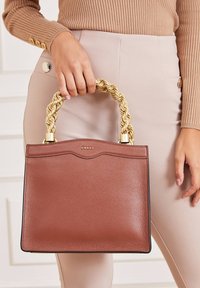 Sac à main en cuir marron texturé avec une poignée tressée dorée épaisse, présentant un motif subtil en forme de vague sur le dessus et un logo doré.