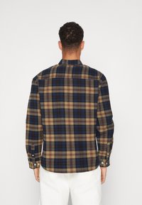 Camisa de franela a cuadros en azul marino, beige y marrón. Cuenta con mangas largas, puños con botones y un dobladillo recto. Tejido texturizado y cálido.