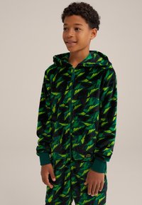 Flis onesie s črno podlago, okrašen zelenimi listnatimi vzorci, s kapuco in zadrgo. Manšete in rob so v enotni zeleni barvi.