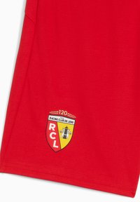 Bañadores deportivos rojos con una tela texturizada. Los detalles notables incluyen un logo en forma de escudo con las inscripciones "RCL" y "Racing Club de Lens".