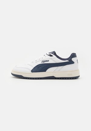 Baskets basses Puma blanches et bleu marine avec fermeture à lacets, bande contrastante et semelle de couleur crème sur fond uni.