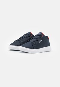Marineblaue Sneakers aus Netzmaterial mit einer weißen Sohle. Sie verfügen über runde Schnürsenkel, ein Logo-Akzent und rote Details an der Ferse.