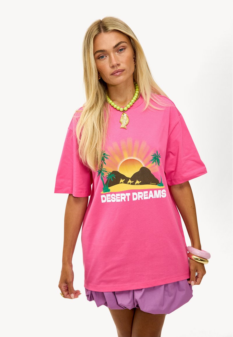 T-shirt en coton rose avec un graphique "DESERT DREAMS", soleil, montagnes et palmiers. Coupe décontractée avec des manches courtes.