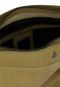 Intérieur d'un sac en cuir tan avec une texture mate et lisse, comportant une fermeture éclair et un emblème d'ancre. Doublé de tissu foncé.