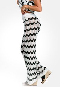 Pantaloni in maglia all'uncinetto bianco e nero con un motivo ondulato, dotati di vita alta e gambe svasate. Abbinati a sandali con zeppa neri.