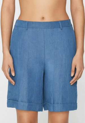 Niebieskie dżinsowe szorty o średniej długości z wywiniętymi brzegami, noszone przez osobę pokazującą obszar od talii do połowy uda.