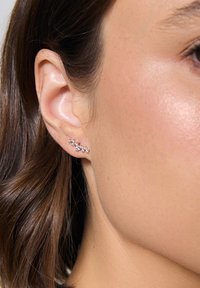 Srebrny klips na ucho z małymi przezroczystymi kamieniami ułożonymi w zakrzywiony kształt. Gładka powierzchnia i polerowane wykończenie, które podkreślają blask klejnotów.