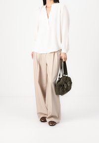 Weiße Langarmbluse mit Teilknopfleiste, kombiniert mit beigen weiten Hosen und einer dunkelgrünen strukturierten Handtasche. Schuhe mit Leopardenmuster.