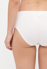 White cotton briefs with elastic waistband. Smooth texture, minimalistic design, and a low-cut leg opening for comfort. Sloggi logo visible.
