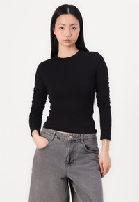 Schwarzes Langarmoberteil mit Rundhalsausschnitt und figurbetontem Schnitt, kombiniert mit hellgrauen weiten Jeans mit Fronttaschen und entspannter Passform.