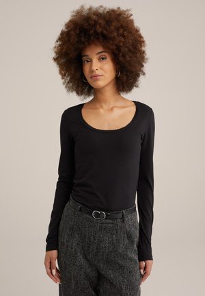 Top negro de manga larga con cuello redondeado y borde con forma de onda, combinado con pantalones grises texturizados y un cinturón negro.