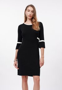Black three-quarter sleeve dress with white trim at neckline and sleeves, ribbed texture, knee-length, fitted silhouette.