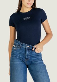 Námořnicky modré tričko s krátkými rukávy, kulatým výstřihem a logem na přední straně. Kombinováno s vysokořezanými modrými džínami z denimu. Hladká texturou látky.