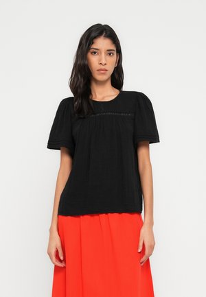 Čierny top s krátkymi rukávmi so zhromaždeným dizajnom, textúrovanou látkou a jemným dekoratívnym prešitím cez hruď. Dopĺňa ho červená sukňa.
