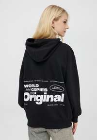 Czarna bluza z kapturem, z białymi grafikami tekstowymi na plecach. Luźny krój z miękką teksturą. Casualowy design z kieszenią z przodu.