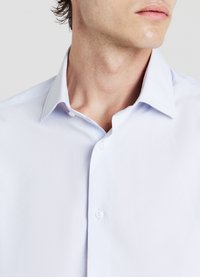 Camicia azzurra chiara, maniche corte, con una texture sottile, chiusura a bottoni e colletto a punta. Presenta sottili righe e tessuto liscio.
