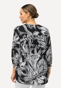 Sort-hvid blomstret bluse med trekvartærmer, samlet ryg og tekstureret stof. Har en løs pasform og bindebånd på ærmerne.