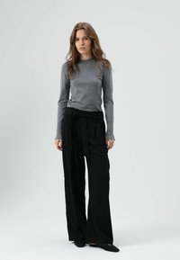 Grijze top met lange mouwen gecombineerd met zwarte, wijd uitlopende broek met strikceintuur, gladde textuur en minimalistisch ontwerp.