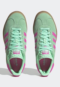 Gröna mockasneakers med rosa ränder, strukturerade detaljer, platta snören och en gummisula i naturfärg. Tungan har en rosa logotypetikett.