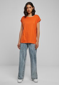 Oranje T-shirt met korte mouwen van katoen, gecombineerd met lichtblauwe denim jeans met wijde pijpen. De outfit heeft een ontspannen pasvorm en een casual stijl.