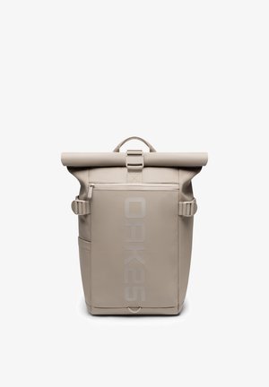 Sac à dos beige à rabat roulé avec poche avant zippée, deux sangles latérales et "OAK25" imprimé verticalement sur le panneau avant.