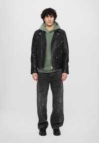 Svart läderbikerjacka, grön hoodie, grå mönstrade jeans, svarta stövlar. Jackan har dragkedjor och fickor; jeansen har detaljerade mönster.