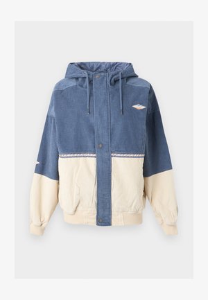 Veste à capuche en velours côtelé bleu et beige avec boutons-pression sur le devant, cordons, deux poches et petits écussons brodés sur la poitrine et la manche.