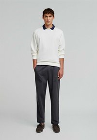 Cămașă albă cu mâneci lungi și guler bleumarin, combinată cu pantaloni gri închis. Ținuta are un croi lejer și detalii minime. Pantofi maro completează aspectul.