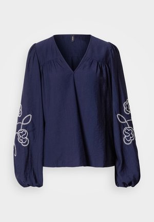 Marineblaue Bluse mit V-Ausschnitt, gerafften Details und langen, gepufften Ärmeln mit weißer Blumenstickerei an den Manschetten.