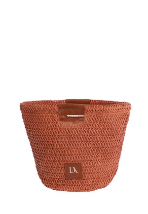 Bolso tote tejido de paja de color óxido con asas recortadas rectangulares y un pequeño parche de logo de cuero marrón en la parte delantera.