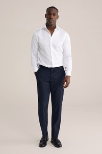 Witte blouse met lange mouwen en een brede kraag, gecombineerd met donkerblauwe broek met krijtstrepen en zwarte loafers. Glad materiaal met een getailleerde pasvorm.