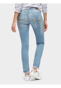 Los vaqueros ajustados de color azul claro presentan una cintura de altura media, puños enrollados y bolsillos traseros bordados con costuras acentuadas. Textura de denim suave.