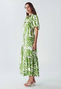 Zelené a bílé vzorované maxi šaty s knoflíkovým zapínáním v přední části, krátkými volánkovými rukávy a stupňovitým lemem. Vyznačují se lehkým materiálem a uvolněným střihem.